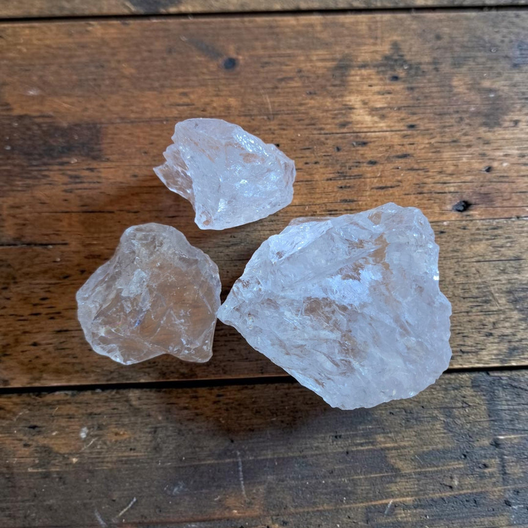 Three raw Satyaloka Quartz crystals from the Satyaloka Monastery in southern India displayed on a rustic wood surface, showing translucent milky-white formations in varying sizes