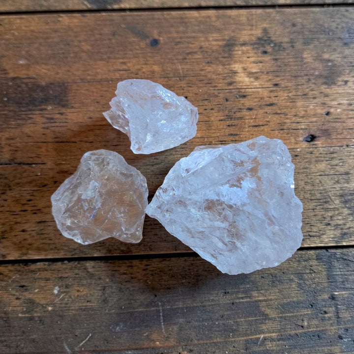 Three raw Satyaloka Quartz crystals from the Satyaloka Monastery in southern India displayed on a rustic wood surface, showing translucent milky-white formations in varying sizes