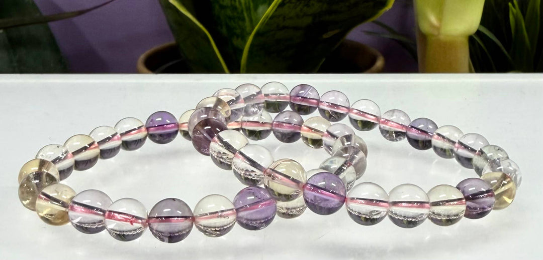 Two natural Ametrine 8mm crystal stretch bracelets crossed on white surface showing translucent purple and golden citrine bead tones