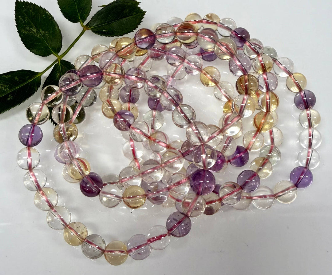 Natural Ametrine crystal bracelets coiled on white surface showing full strand of 8mm amethyst citrine beads with purple and golden tones