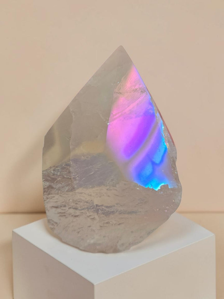 Angel Aura Rose Quartz polished tower point approximately 2.5 inches tall showing vivid rainbow iridescence in pink, blue, and gold from platinum silver and gold bonding, displayed on a white square base