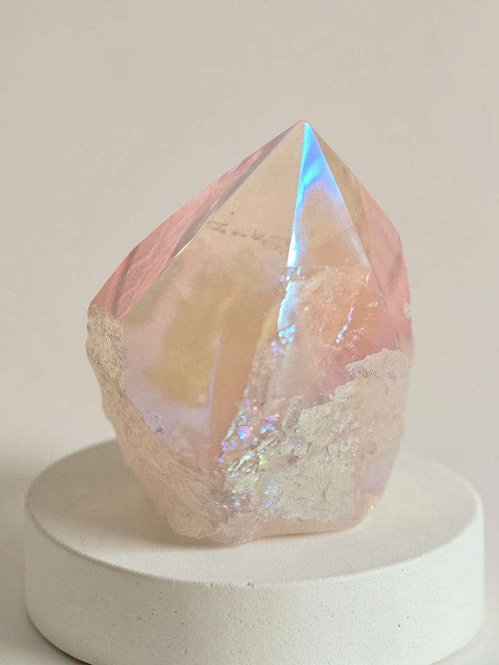 Angel Aura Rose Quartz polished tower point approximately 2.5 inches tall showing vivid rainbow iridescence in pink, blue, and gold from platinum silver and gold bonding, displayed on a white ceramic base