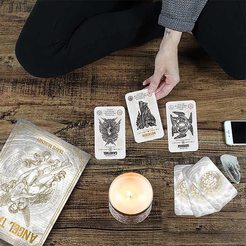 Person doing an Angel Tarot card reading on a wooden surface with candle, crystal point and gold summoning seal pouch