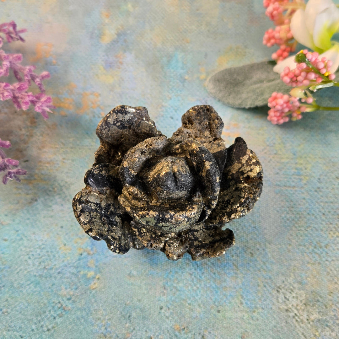 Hand-carved black pyrite flower crystal with gold metallic flecks, styled with lavender and botanicals on painted blue surface
