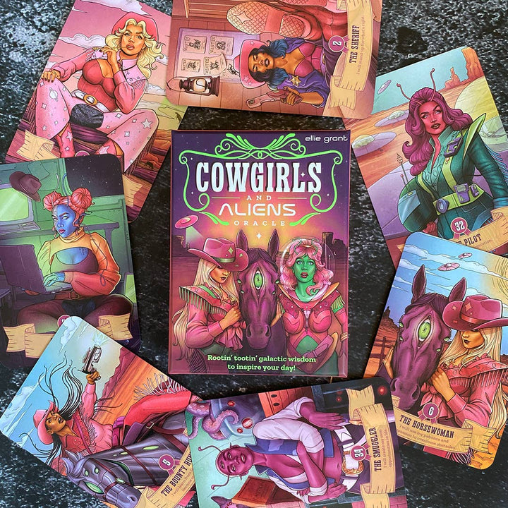 Cowgirls and Aliens Oracle deck box by Ellie Grant surrounded by 10 cards fanned out on a dark surface, showing characters including The Sheriff (2), The Pilot (32), The Horsewoman (6), The Smuggler (30), and The Bounty Hunter (8)