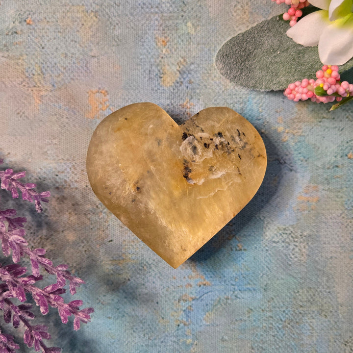 Golden mica polished heart crystal for Solar Plexus healing, styled on painted blue surface with lavender and flowers