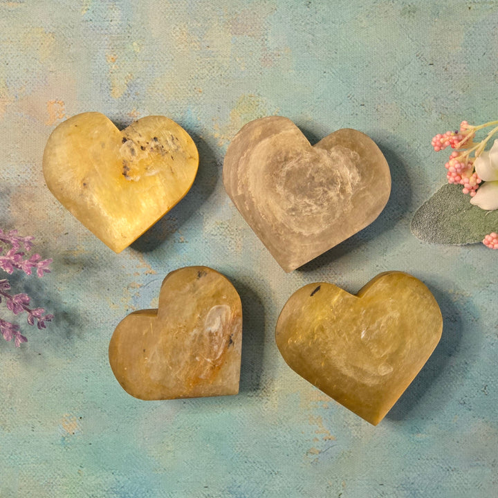 Four golden mica heart crystals showing natural color variation from deep gold to pale cream, styled with botanicals