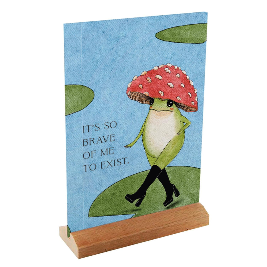  Little Frog affirmation card in a wooden stand, showing a frog in black boots with the message “It’s so brave of me to exist.”