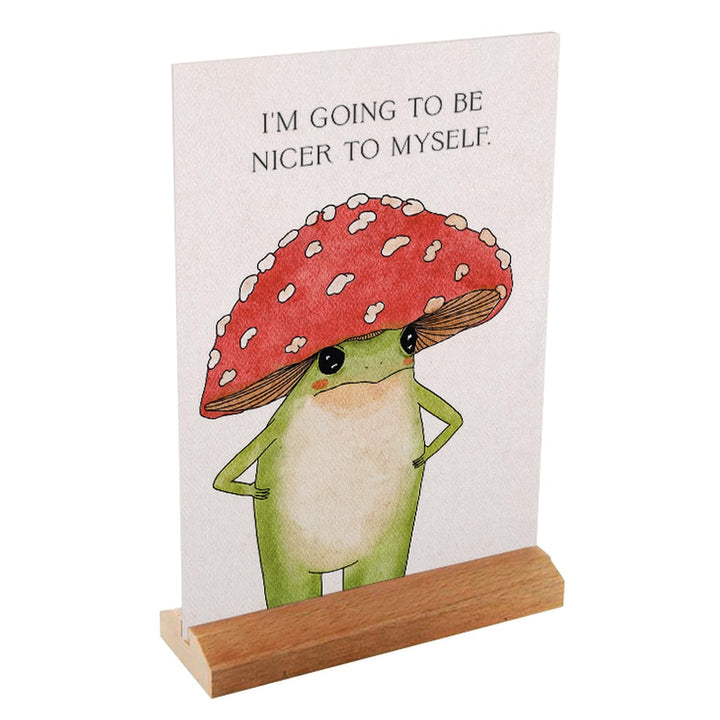 Little Frog affirmation card in a wooden stand, featuring a mushroom-hatted frog and the message “I’m going to be nicer to myself.”