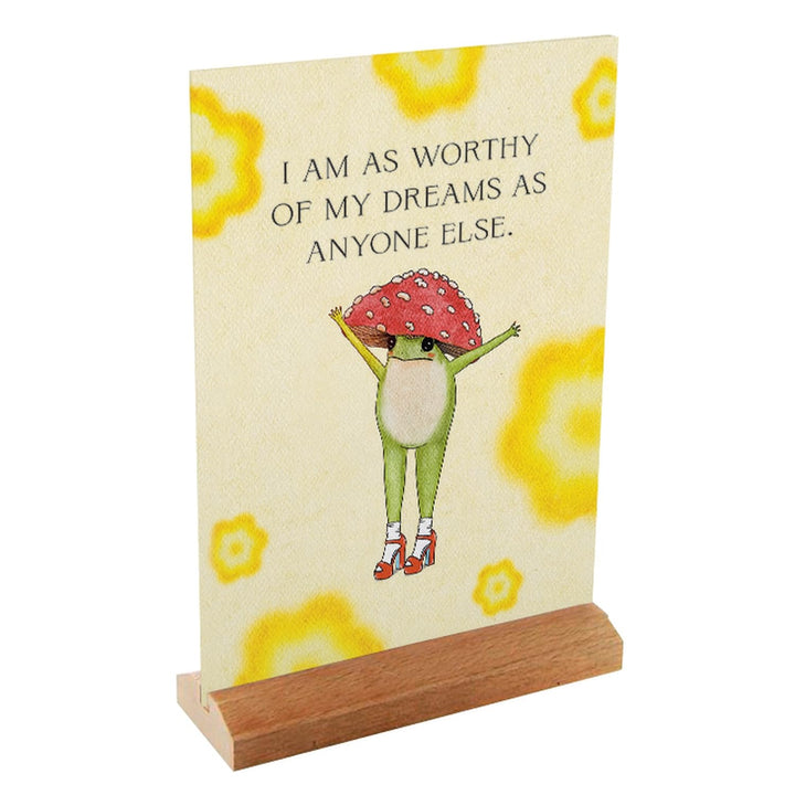 Little Frog card in a wooden stand, showing a frog with raised arms and the affirmation “I am as worthy of my dreams as anyone else.”