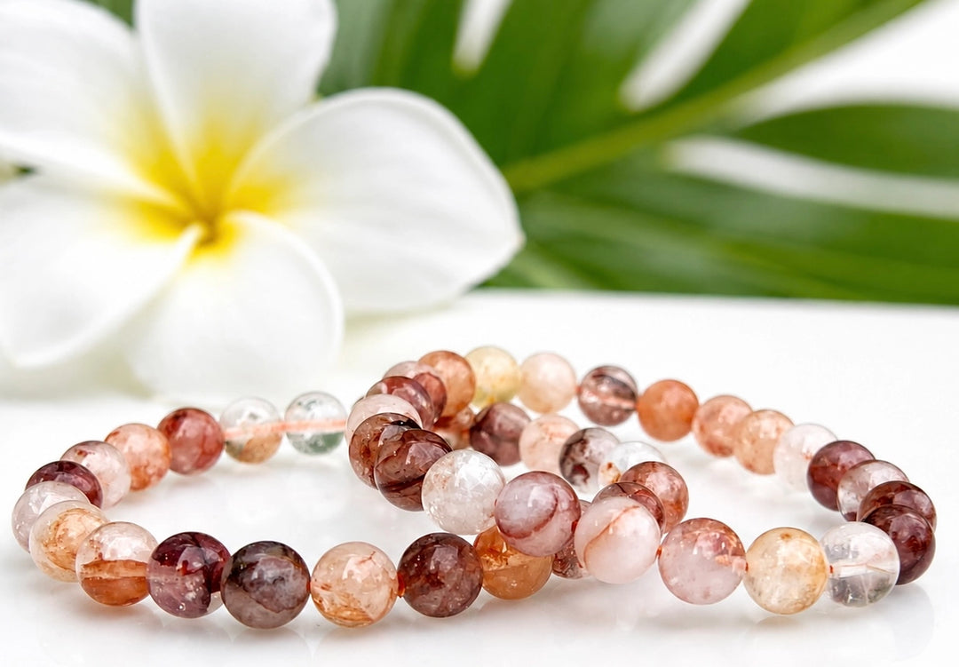 Two natural Hematoid Fire Quartz 8mm stretch bracelets laid flat beside a white plumeria flower