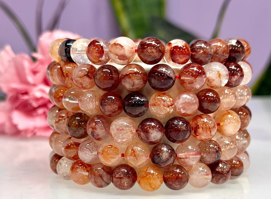 Stack of natural Hematoid Fire Quartz 8mm crystal stretch bracelets showing warm red, amber, and blush bead variations