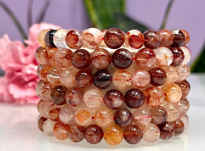 Stack of natural Hematoid Fire Quartz 8mm crystal stretch bracelets showing warm red, amber, and blush bead variations