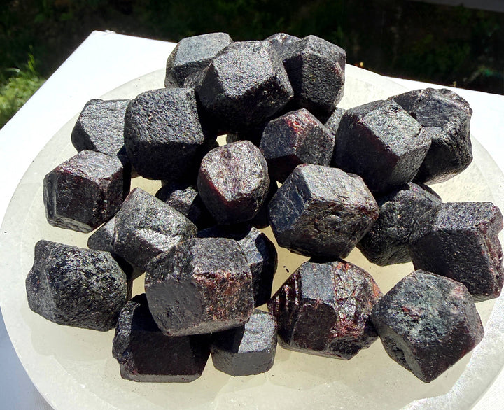 Pile of natural rough garnet crystals in dodecahedron shape on white plate in sunlight