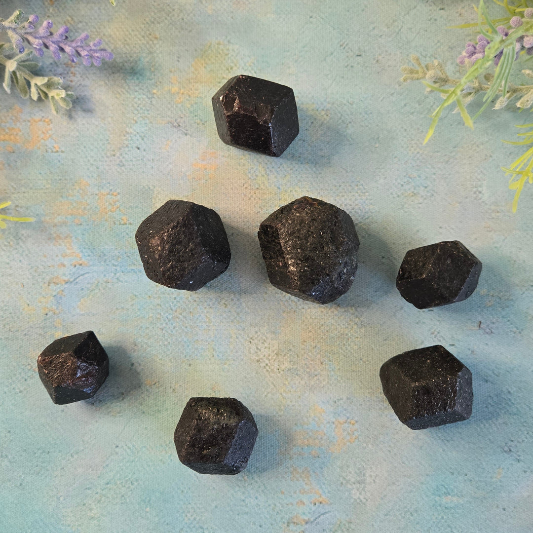 Seven small natural rough garnet crystals scattered on blue background with lavender accents