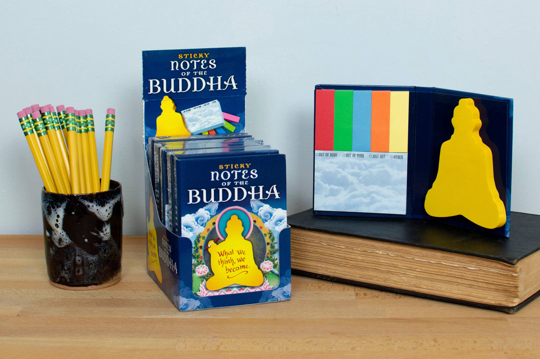 Notes of the Buddha sticky notes booklet open on stacked books beside pencil cup on wooden desk showing Buddha-shaped note and cloud checkbox notes
