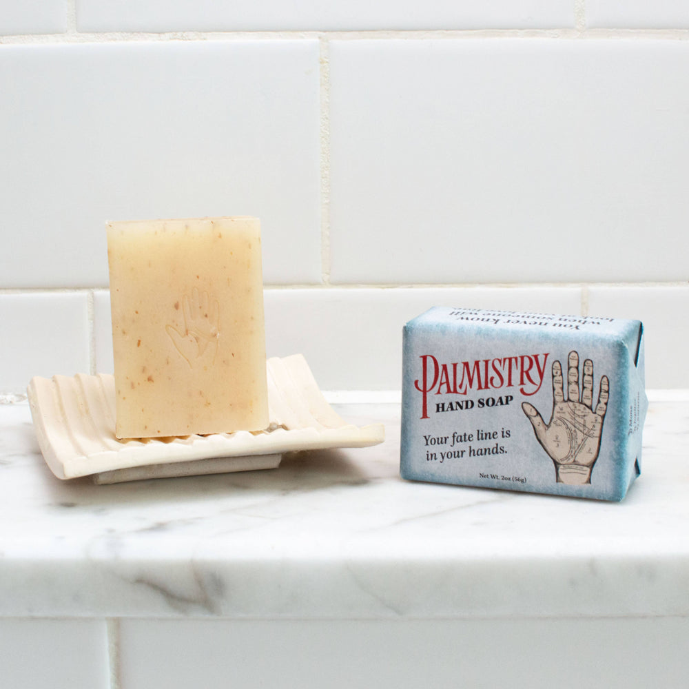 Palmistry shea butter oatmeal soap bar on white soap dish beside palmistry gift box on marble bathroom counter