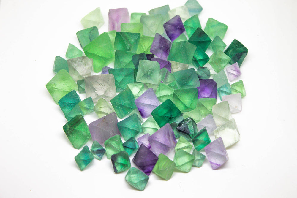 Overhead view of a pile of natural rainbow fluorite octahedrons in green, purple, and clear tones on a white background