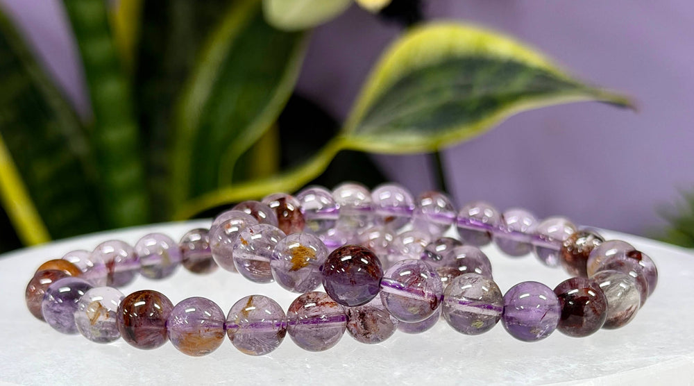 Natural Super 7 crystal stretch bracelet 8mm round beads with purple amethyst and rutile inclusions on white surface