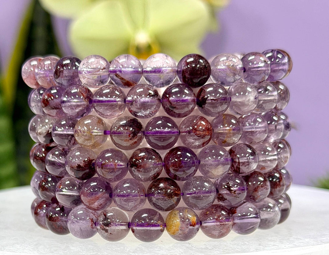 Super 7 crystal stretch bracelets stacked showing purple amethyst and smoky quartz inclusions, 8mm natural Melody's Stone beads