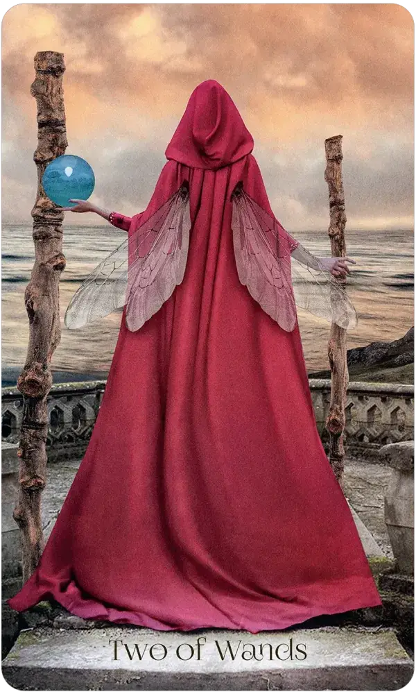 When Women Had Wings Tarot — Two of Wands card featuring a red-cloaked winged woman holding a glowing blue orb between two wooden wands overlooking the ocean