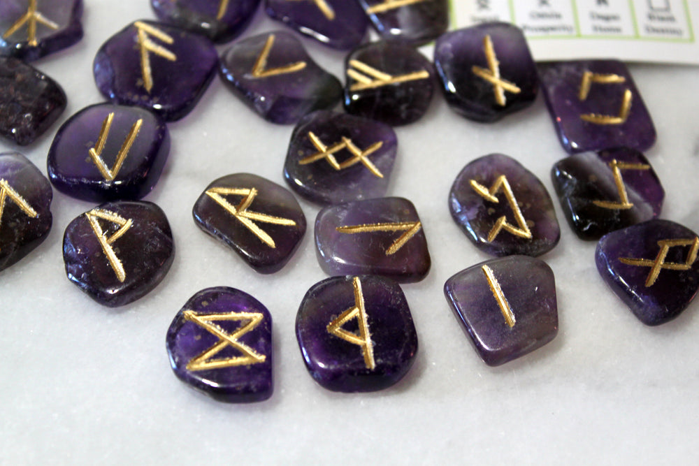 Engraved amethyst Norse rune stones spread out alongside Elder Futhark reference card