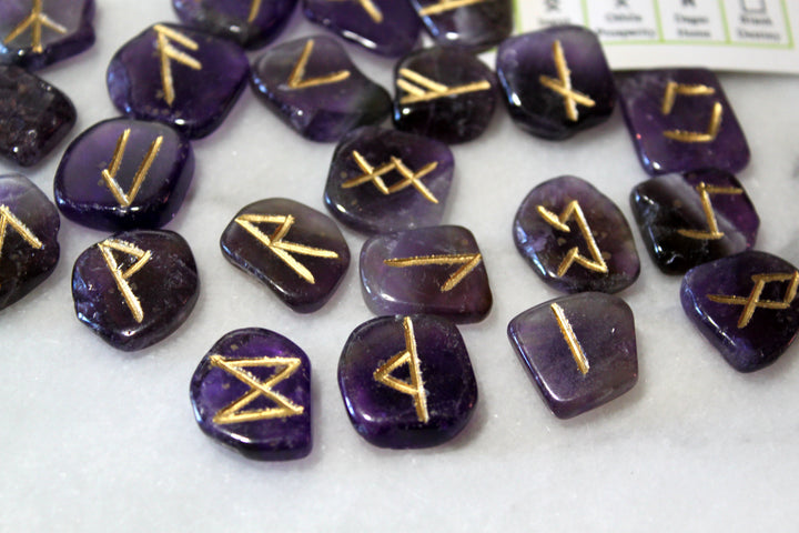 Engraved amethyst Norse rune stones spread out alongside Elder Futhark reference card