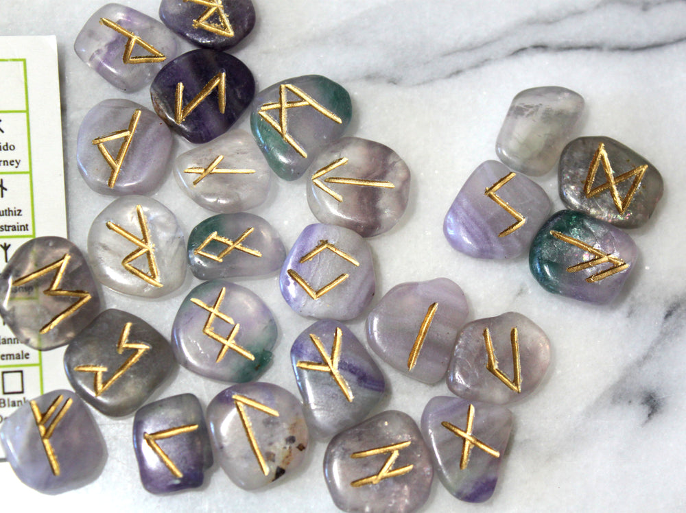 Engraved fluorite Norse rune stones spread out alongside Elder Futhark reference card